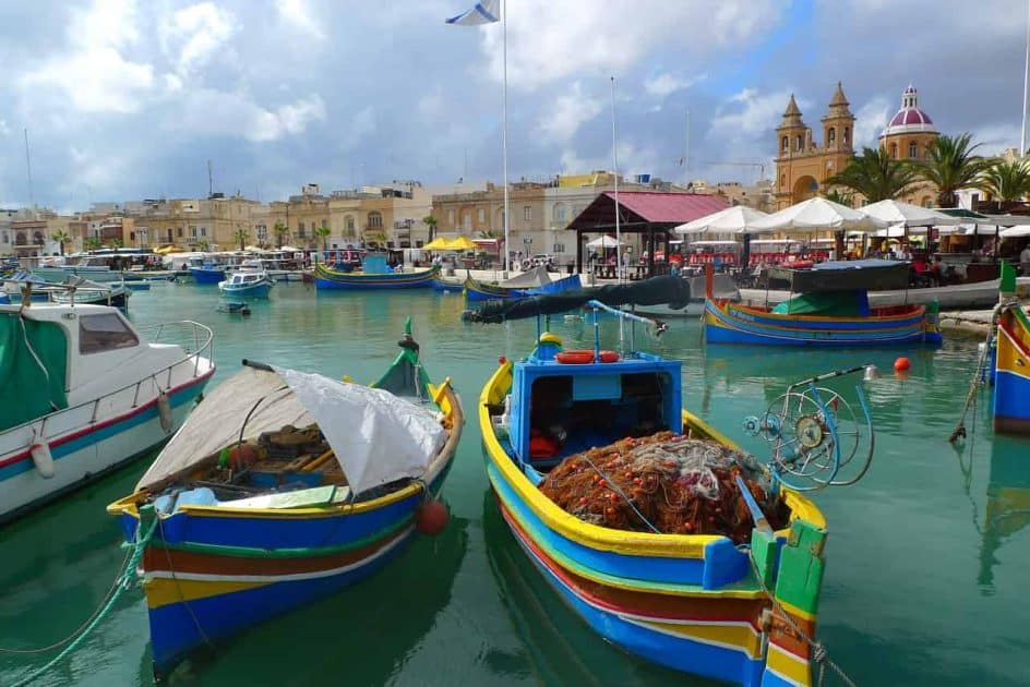 Qué ver en Malta - Luzzus en el puerto de Marsaxlokk, con la Iglesia de Nuestra Señora del Rosario al fondo Qué ver en Malta Luzzus en el puerto de Marsaxlokk, con la Iglesia de Nuestra Señora del Rosario al fondo